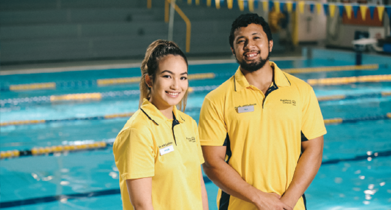 female and male lifeguard smiling and standing in front of pool