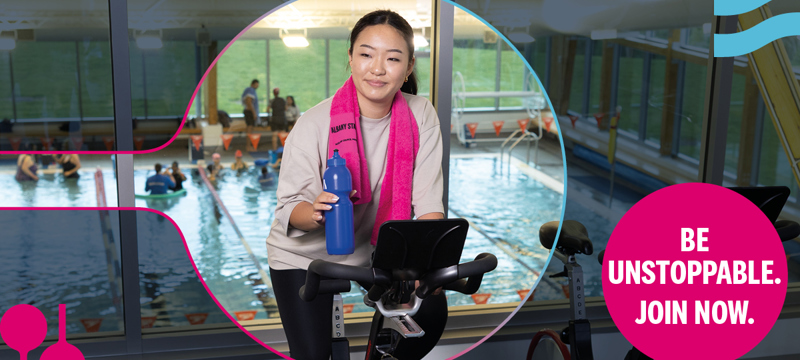 Young woman riding spin bike holding drink bottle with pool in background